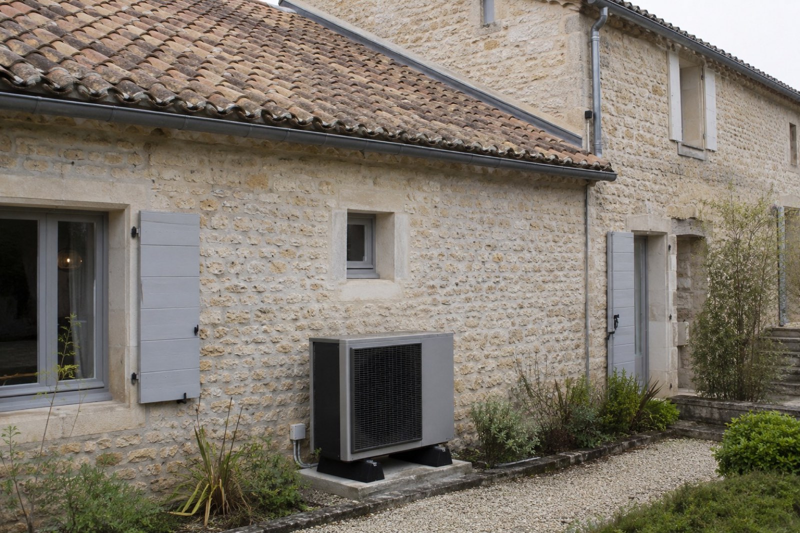 Maison en pierre équipée d'une unité extérieure pour comparer climatisation, pompe à chaleur et isolation